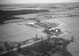The Schimelpfenig farm, viewed from the southwest, was one of 56 farms located on the Fermilab site prior to the start of construction of accelerators. It was located on the corner of Giese and Kautz Road. Scientists built Fermilabs Booster accelerator at the center of the circular area just above the farm.